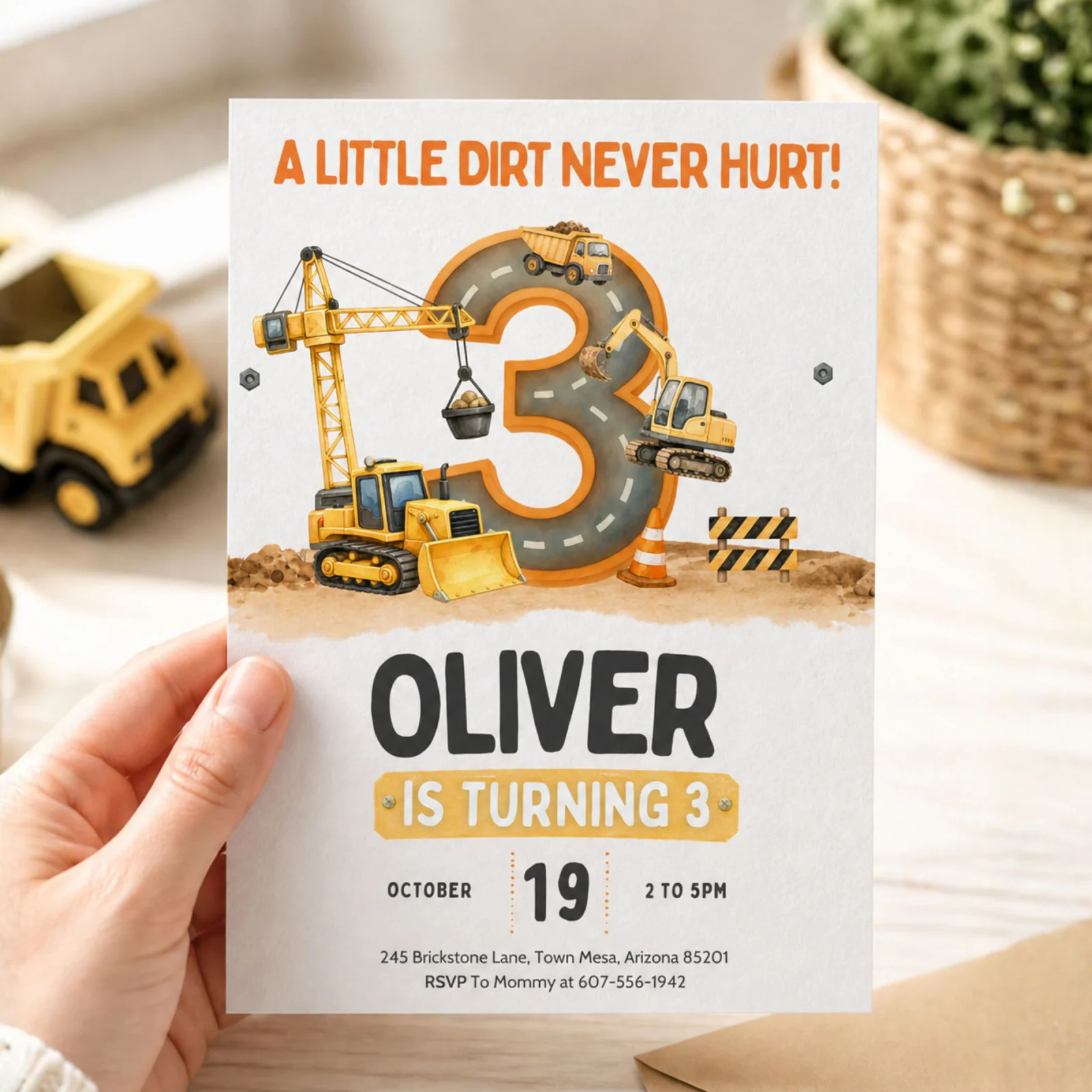Construction 3rd birthday invitation held in hand, showing a dump truck and 'Oliver is turning 3' design.
