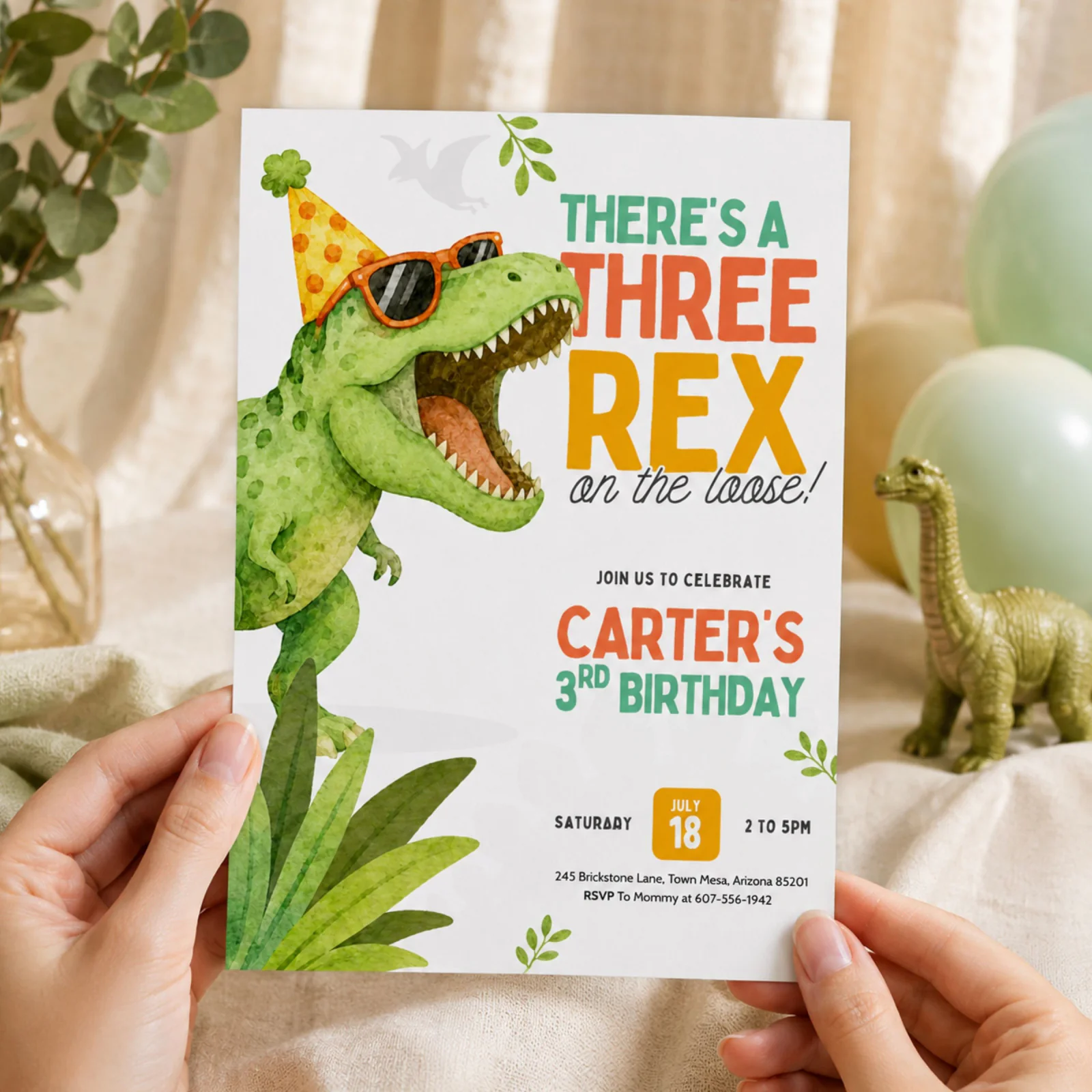 Dinosaur Birthday Invitation held in hands, featuring a green Three Rex in shades and party hat, an editable Canva template.