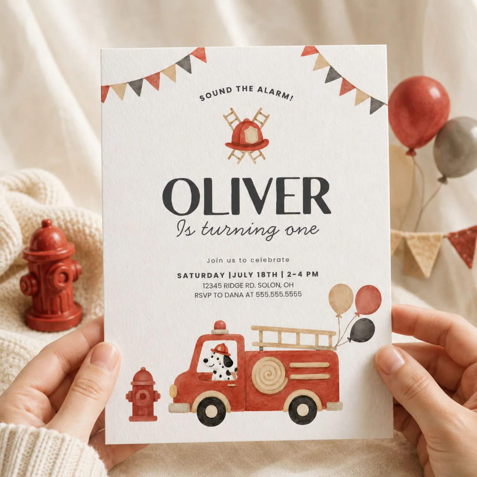 Fire Truck Birthday Invitation held in hands, featuring a watercolor red fire engine, Dalmatian, and bunting flags.