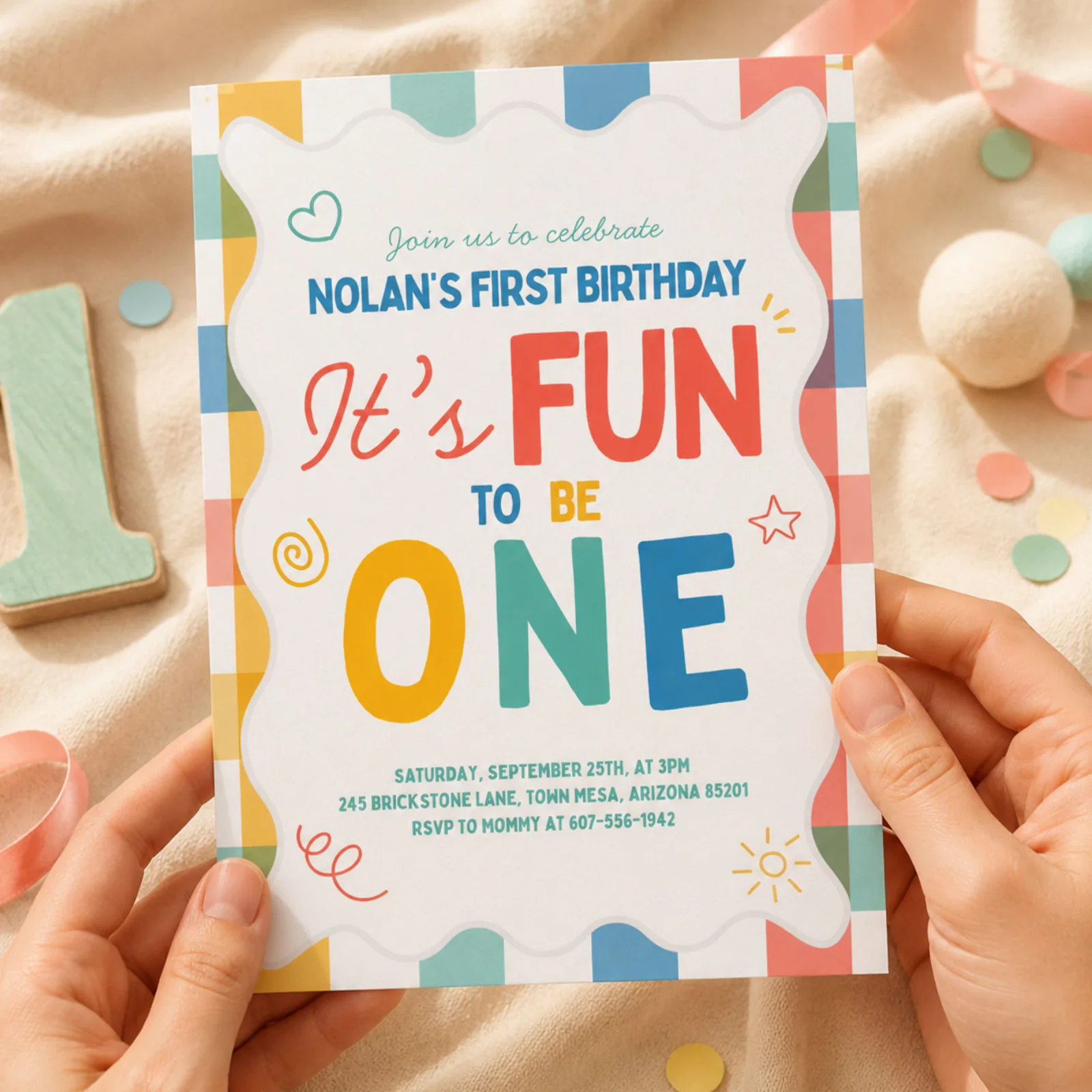 Fun To Be One birthday invitation held in hands, featuring colorful gingham and playful doodles.