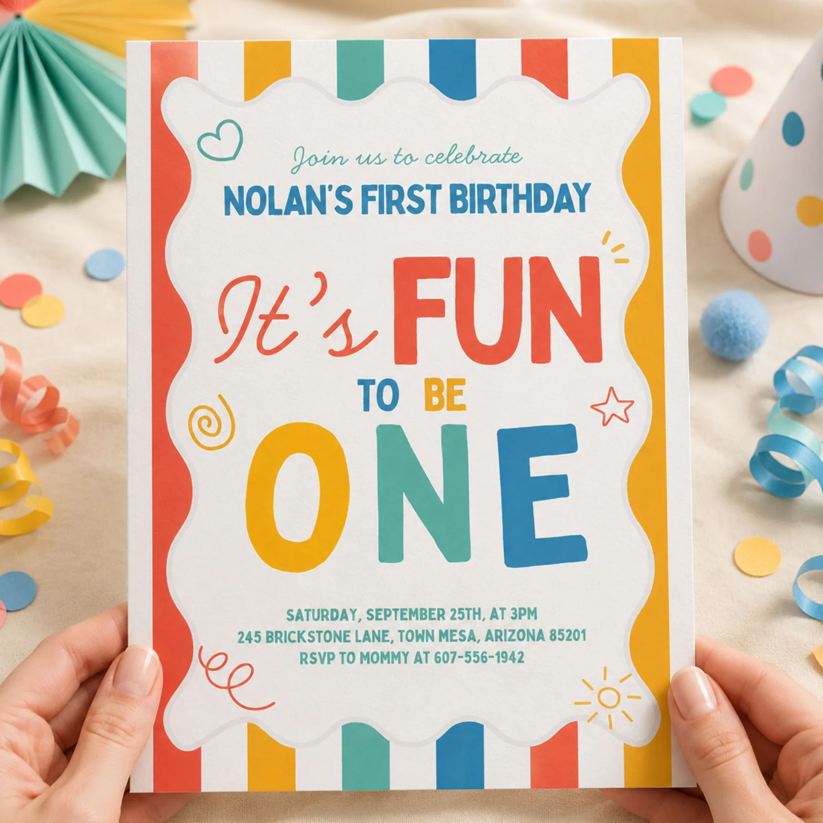 Fun To Be One birthday invitation held in hands, featuring colorful stripes and playful doodles.