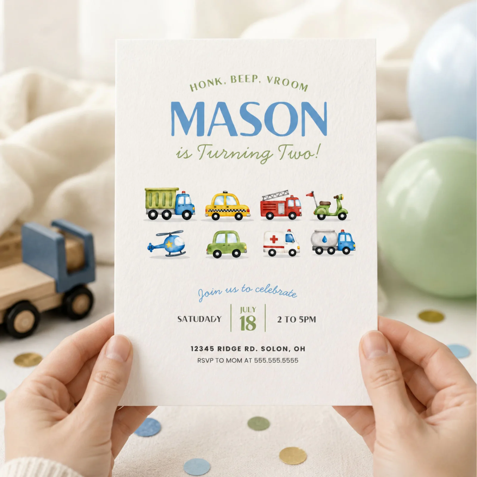 Transportation birthday invitation held in hands, featuring watercolor trucks, cars, and a helicopter.